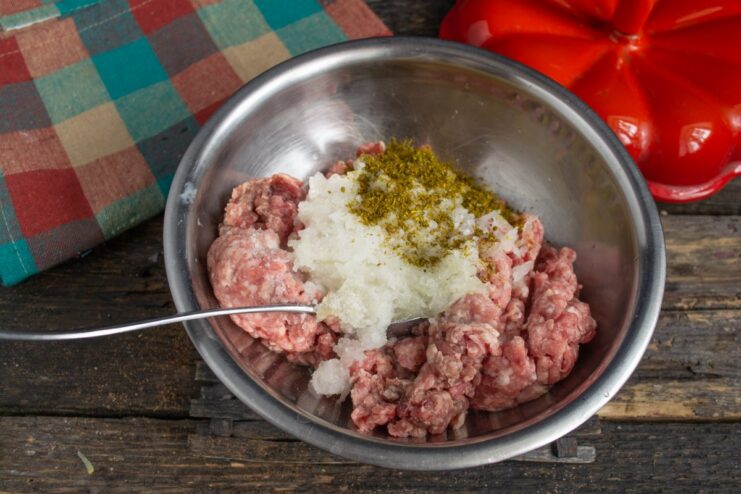 Seasoning the meatball mixture Salt and spices being added to the ground meat mixture.