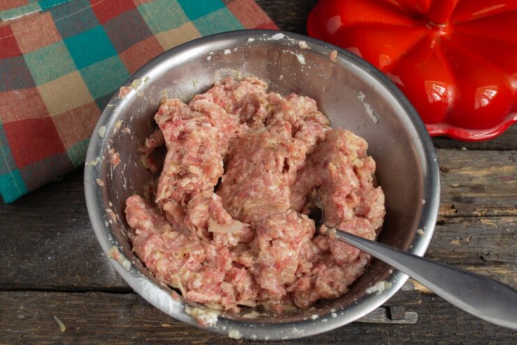 Thoroughly mixing the ground meat for tender meatballs Hands mixing the ground meat, egg, onion, and spices in a bowl.