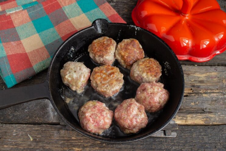 Browning the meatballs in a pan Meatballs being fried in a pan until golden brown on all sides.