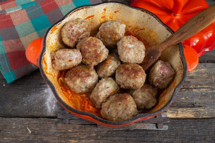 Combining the fried meatballs with the vegetable sauce Fried meatballs being placed into the skillet with the vegetable sauce.