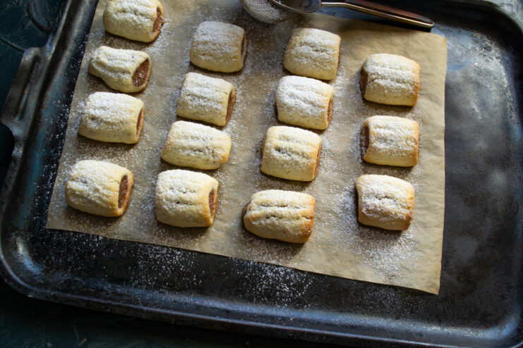 Dusting freshly baked cookies with powdered sugar Warm Nascondini cookies on a baking sheet being dusted with powdered sugar.