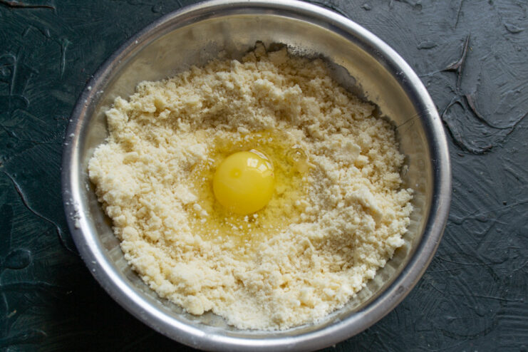 Adding an egg to the flour and butter mixture An egg cracked into a well in the middle of a flour and butter mixture.