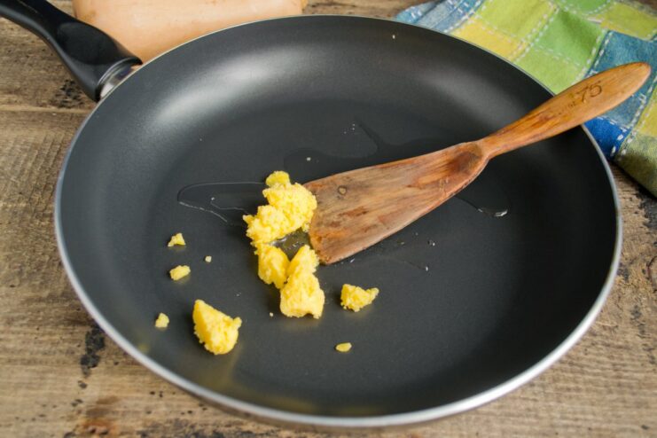 Start by melting ghee in a non-stick skillet for a rich flavor. Melting a piece of ghee in a black non-stick skillet.