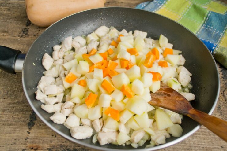 Adding diced pumpkin and zucchini to the skillet to cook with the chicken. Diced pumpkin and zucchini being added to the chicken and onions in the pan.