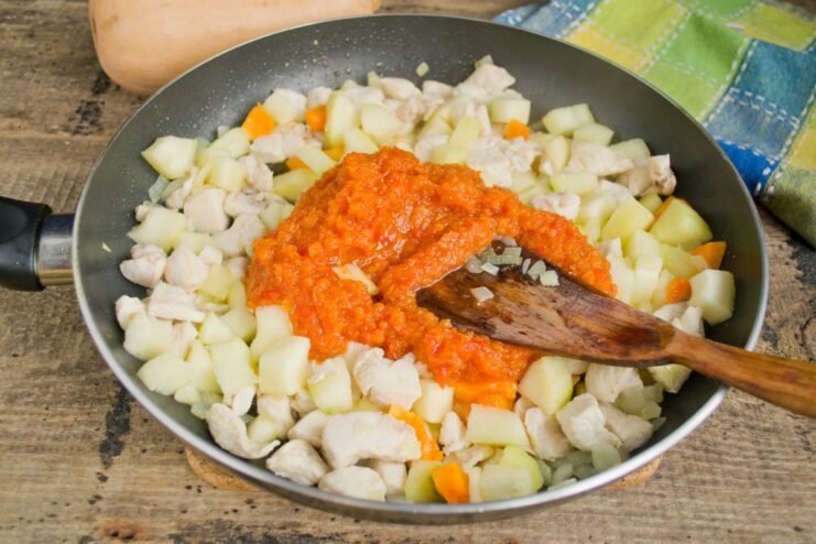 Stirring in zucchini adjika to create a rich and flavorful sauce. Adding a spoonful of red zucchini adjika to the vegetable and chicken mixture in the skillet.
