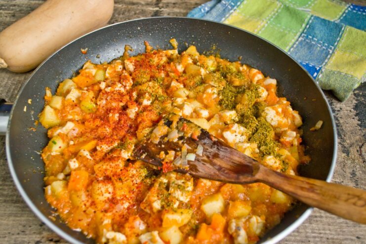 Simmering the stew and adding spices like khmeli-suneli and paprika for aroma. The stew simmering in the pan after adding spices.