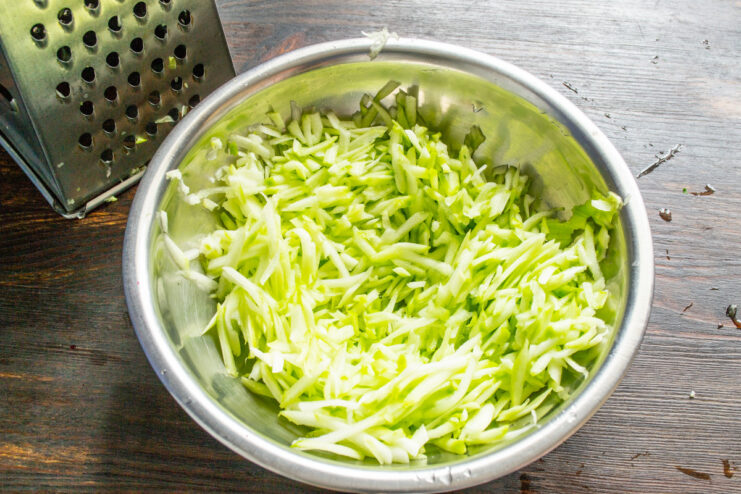 Grating Zucchini for Fritters - Step-by-Step Close-up of zucchini being grated on a coarse grater into a bowl.