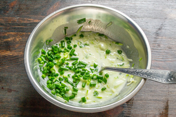 Mixing Milk and Onions into the Fritter Batter Pouring milk into the zucchini and herb mixture, with chopped green onions.