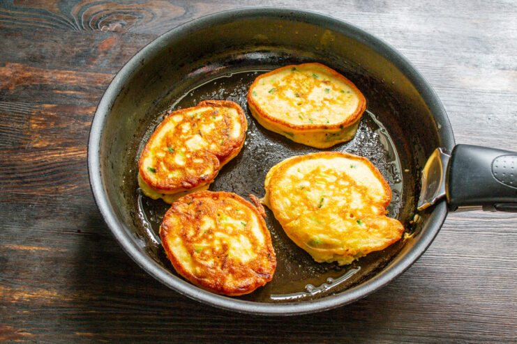 Flipping and Frying the Zucchini Fritters Until Golden Zucchini fritters being fried in a pan, showing their golden-brown underside.