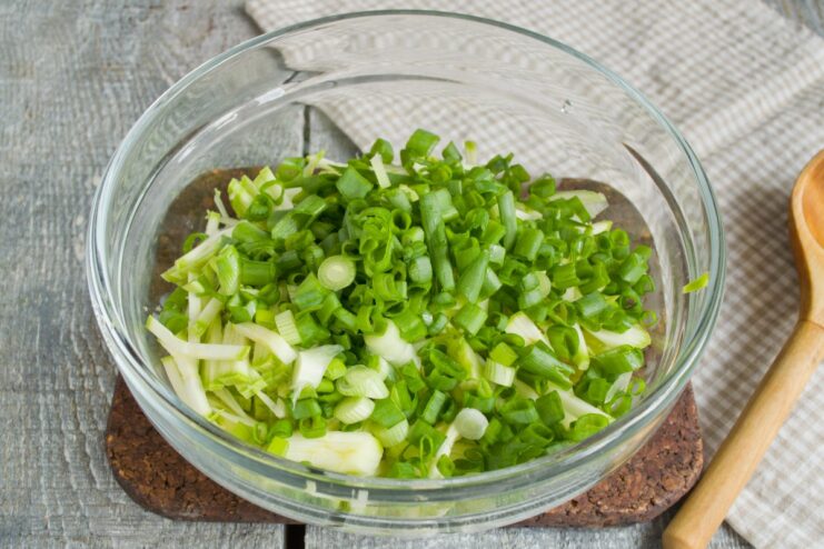 Adding Freshness: Chopped Green Onions for Zucchini Fritters Chopped green onions being added to a bowl of grated zucchini.