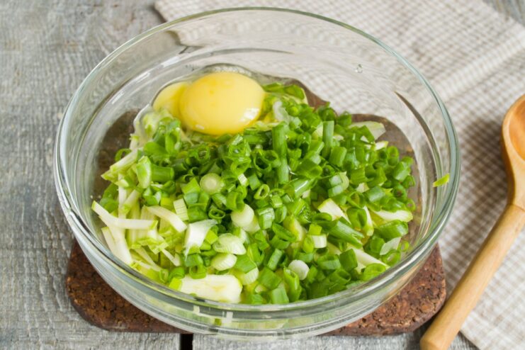 Binding the Fritter Batter: Mixing in the Eggs Eggs being mixed into the zucchini and green onion mixture in a bowl.