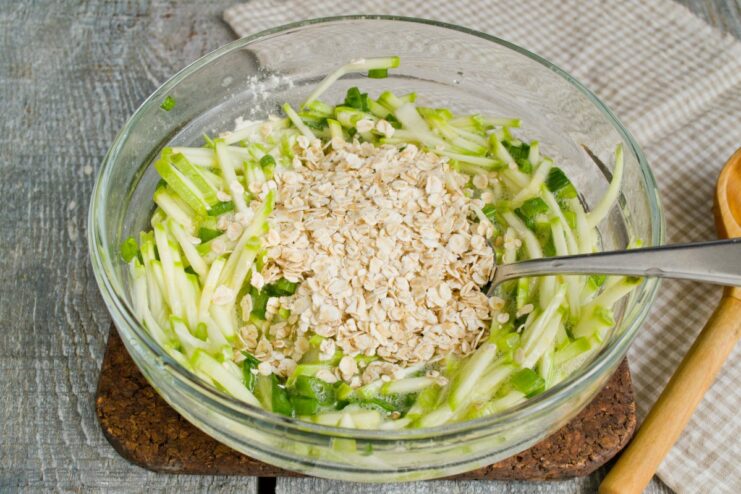 For a Healthy Twist: Adding Rolled Oats to the Batter Rolled oats being added to the zucchini fritter batter in a bowl.