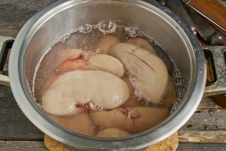 Changing the water and rinsing is crucial for odor-free kidneys. Rinsing partially boiled pork kidneys in a colander under running water.
