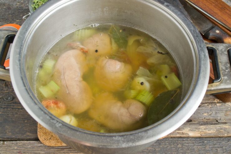 Simmering the kidneys with spices infuses them with flavor. A pot of pork kidneys simmering with spices and vegetables.