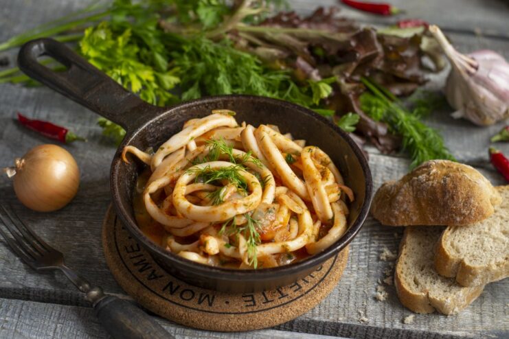 A bowl of ready-to-eat squid in tomato sauce, garnished with fresh herbs.