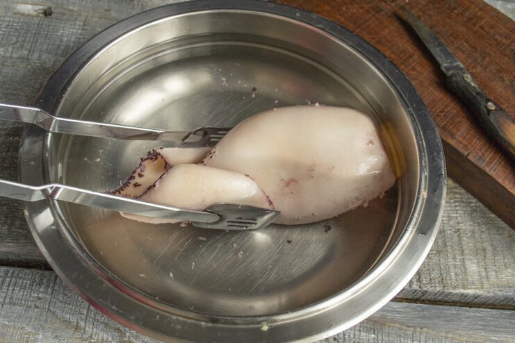 Shocking the squid in cold water to stop the cooking process Cooked squid being transferred from a pot to a bowl of cold water.
