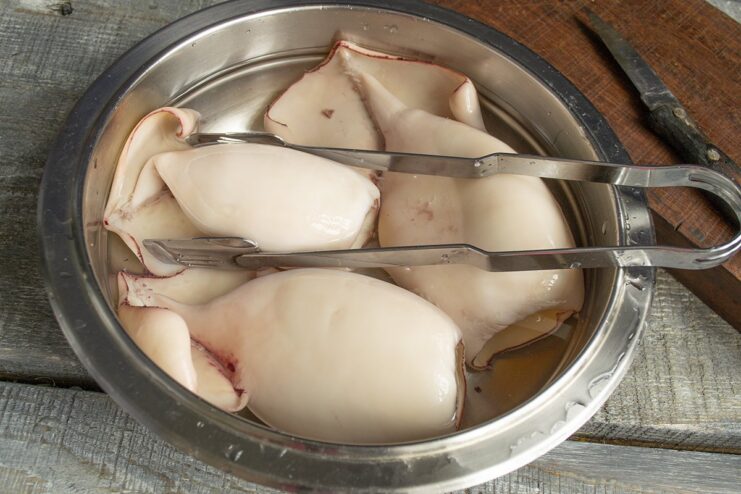 Step-by-step guide on how to clean a cooked squid A person cleaning a cooked squid under running water.