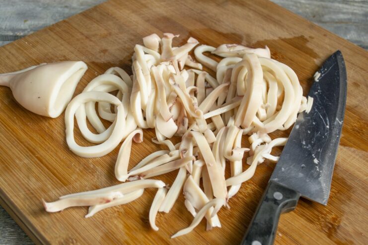 Slicing boiled squid into rings and strips for the sauce Boiled squid being cut into rings on a cutting board.