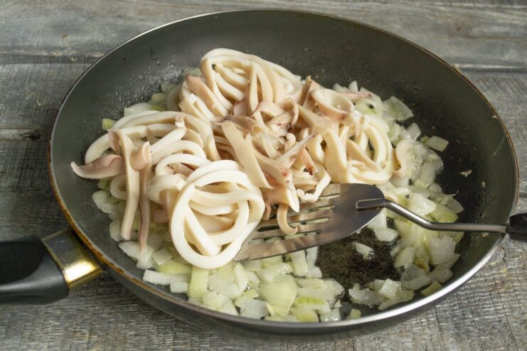Adding sliced squid to the sautéed onions and garlic Sliced squid rings being added to a pan with translucent onions.