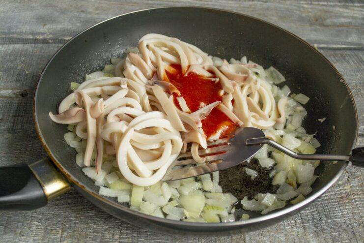 Adding tomato purée to create the sauce Tomato purée being added to the squid and onions in the pan.