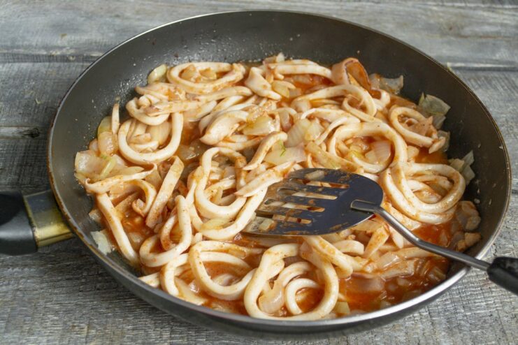 Cooking the squid in tomato sauce over high heat Squid simmering in tomato sauce in a pan on the stove.
