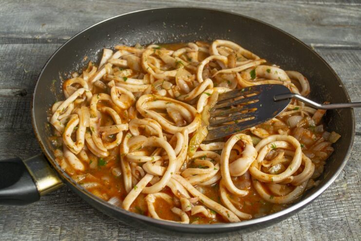Final steps for cooking squid in tomato sauce Stirring the squid in tomato sauce with fresh dill in a pan.