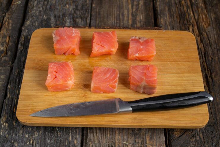 Slicing lightly salted salmon for canapés A close-up of a knife slicing a piece of lightly salted salmon on a cutting board.