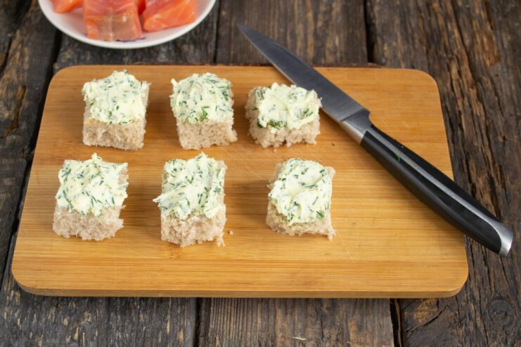Spreading dill butter on toasted bread Toasted bread cubes being spread with a layer of green dill butter.
