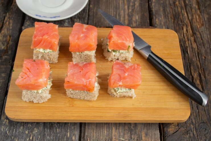 Assembling the canapé: adding salmon Assembling the canapé: placing a slice of salmon on top of the dill buttered toast.
