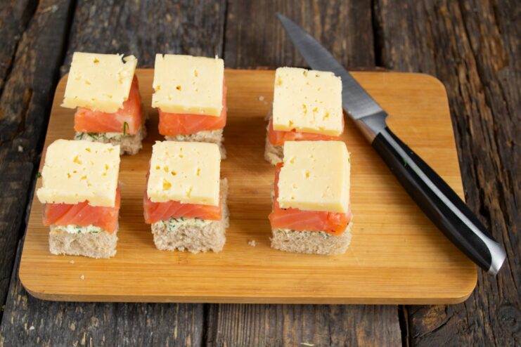 Adding a layer of cream cheese to the canapé Adding a small square of cream cheese on top of the salmon slice.