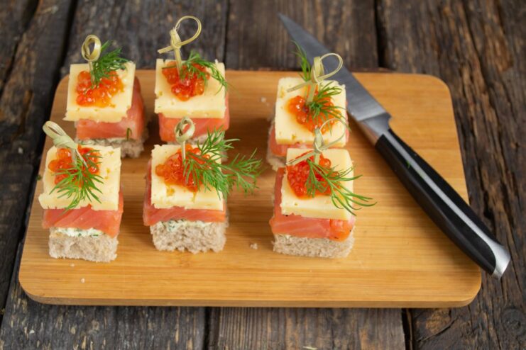 Securing the canapé with a bamboo skewer A hand piercing a fully assembled salmon canapé with a bamboo skewer.
