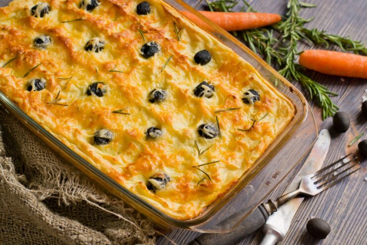 A finished potato casserole with chicken, cheese, and olives in a white baking dish, garnished with fresh herbs.