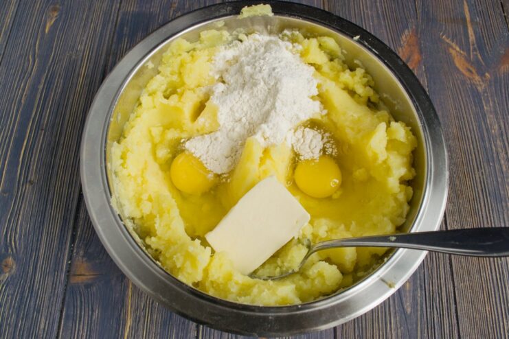 Enriching the Mashed Potatoes for a Stable Casserole Topping A bowl of mashed potatoes with two cracked eggs, a pat of butter, and a spoonful of flour on top.