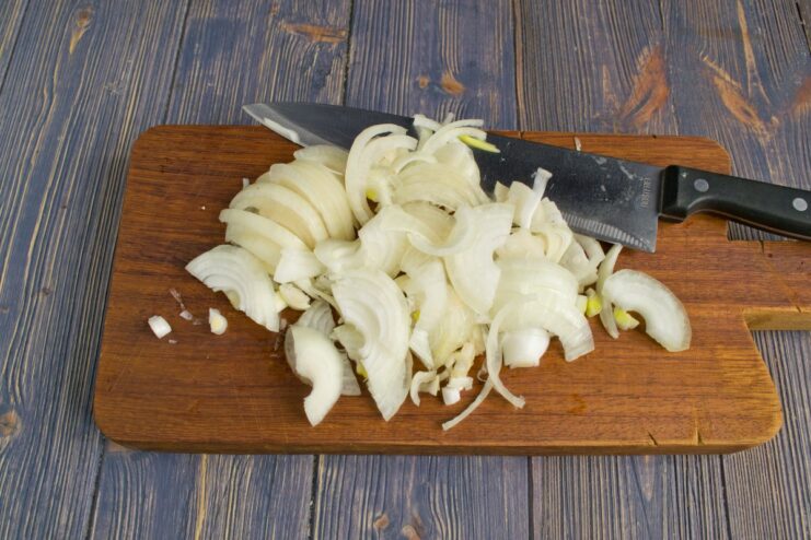 Finely Chopping Onions for the Savory Casserole Filling A hand holding a knife, finely chopping a yellow onion on a wooden cutting board.