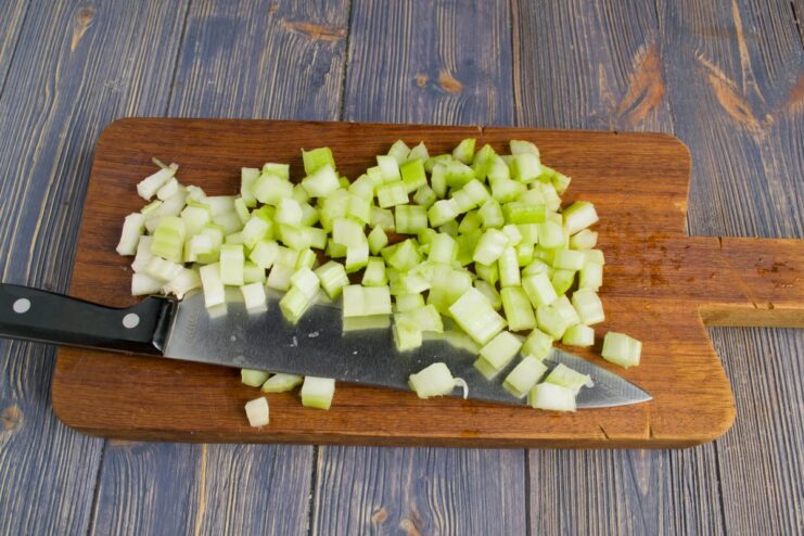 Dicing Celery Stalks to Add Flavor and Texture Fresh celery stalks being diced into small cubes on a cutting board.