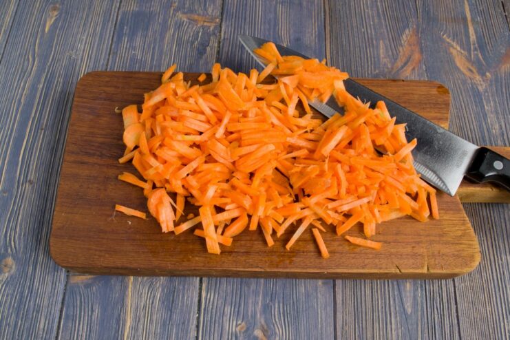 Finely Chopping Carrots for the Casserole Base Bright orange carrots being finely chopped on a cutting board.
