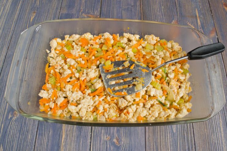 Layering the Chicken and Vegetable Filling in the Baking Dish The cooked chicken and vegetable filling spread evenly on the bottom of a white baking dish.