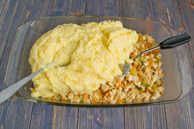Topping the Filling with a Generous Layer of Mashed Potatoes A layer of smooth mashed potatoes being spread over the chicken filling in the baking dish.
