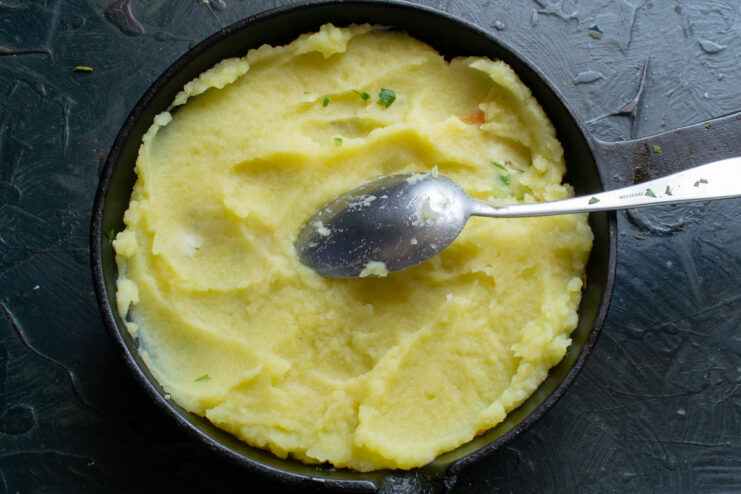 Spreading mashed potatoes over the fish layer A layer of creamy mashed potatoes being spread evenly over the fish and vegetable filling in a pan.