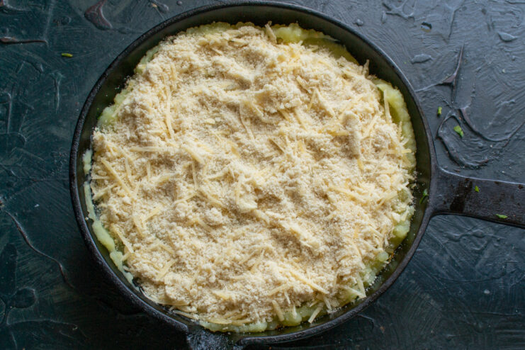 Sprinkling the cheese and breadcrumb topping over the casserole A hand sprinkling the cheese and breadcrumb mixture over the mashed potato layer of the casserole.