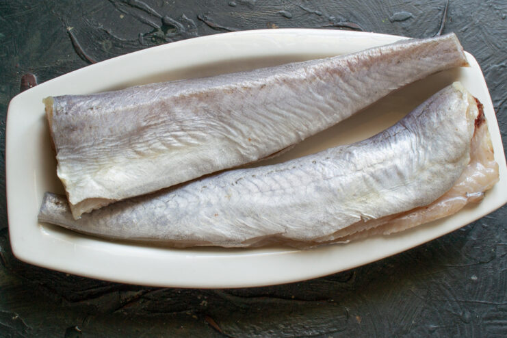 Preparing the fish: gutting, trimming fins, and rinsing A whole hake fish being cleaned on a cutting board before cooking.