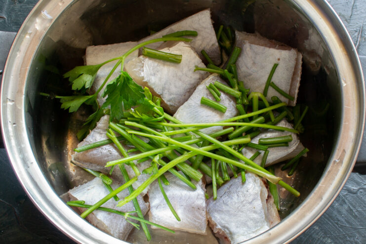 Cutting the hake into large pieces for boiling Raw hake fish cut into large chunks on a wooden cutting board.
