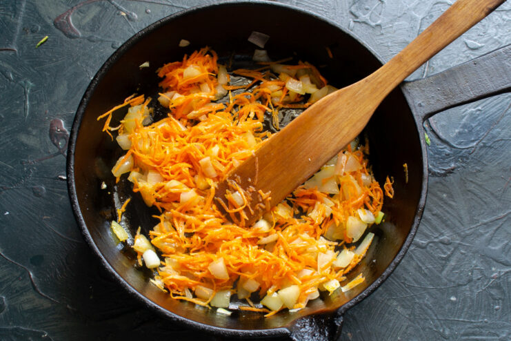 Adding grated carrots to the sautéed onions Grated carrots and chopped onions being cooked together in a skillet.