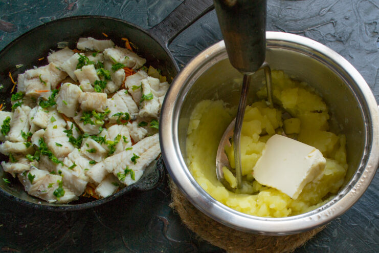 Mashing boiled potatoes with a potato masher A hand using a potato masher to make mashed potatoes in a pot.