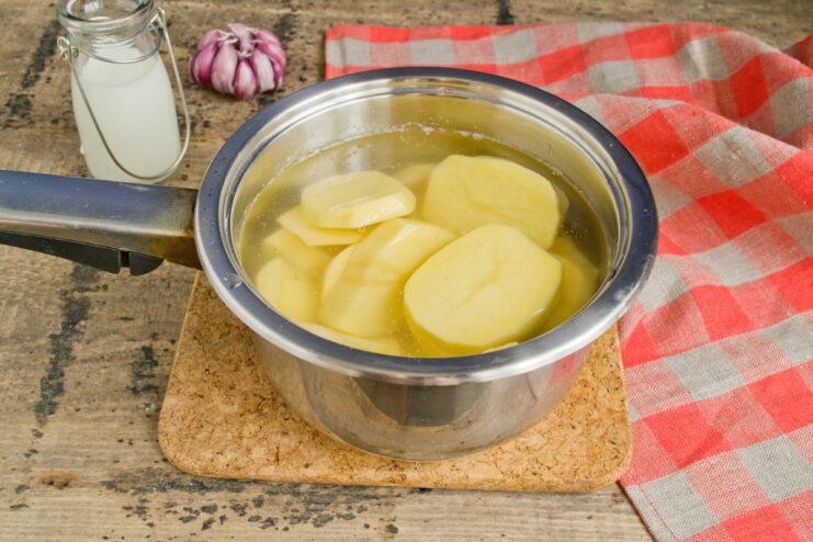Sliced potatoes and garlic boiling in a pot of water on the stove.