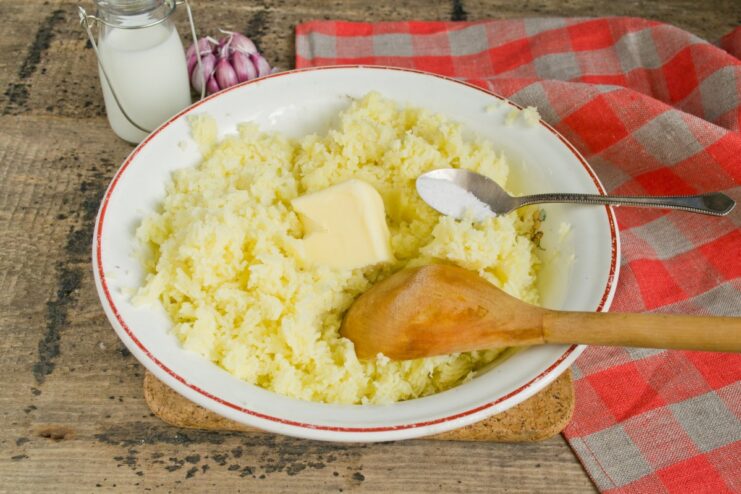 A pat of butter and a sprinkle of salt being added to the riced potatoes in a bowl.