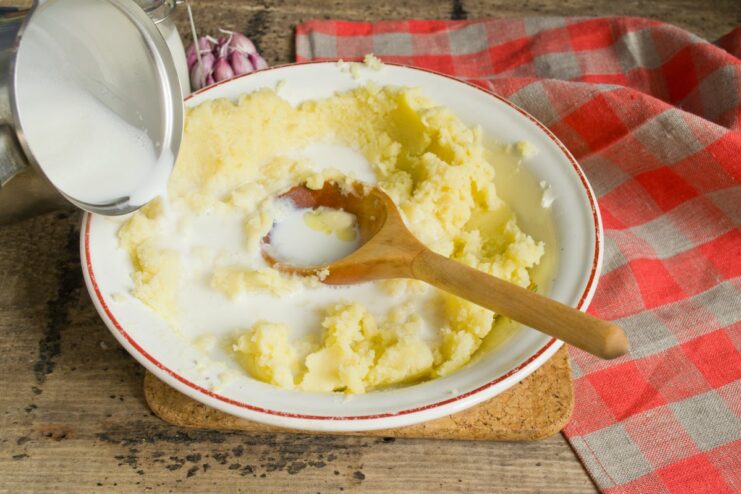 Hot milk being poured from a saucepan into the bowl of mashed potatoes.