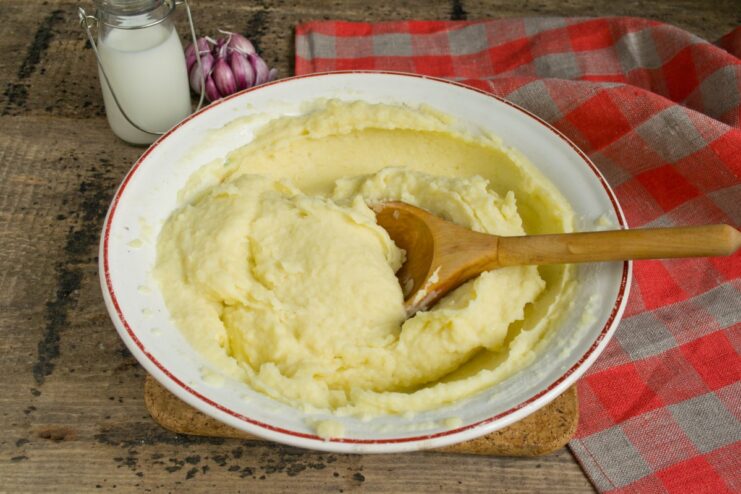 Mashed potatoes being whipped with a spoon in a glass bowl to make them fluffy.