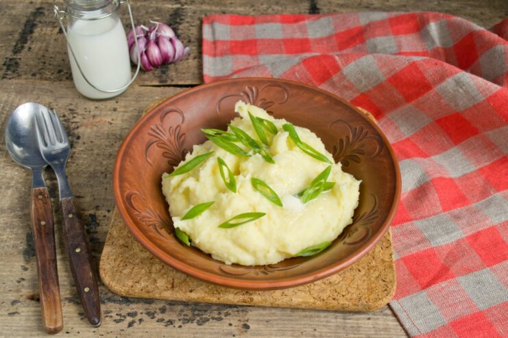 A finished bowl of creamy mashed potatoes, topped with butter and fresh green onions.