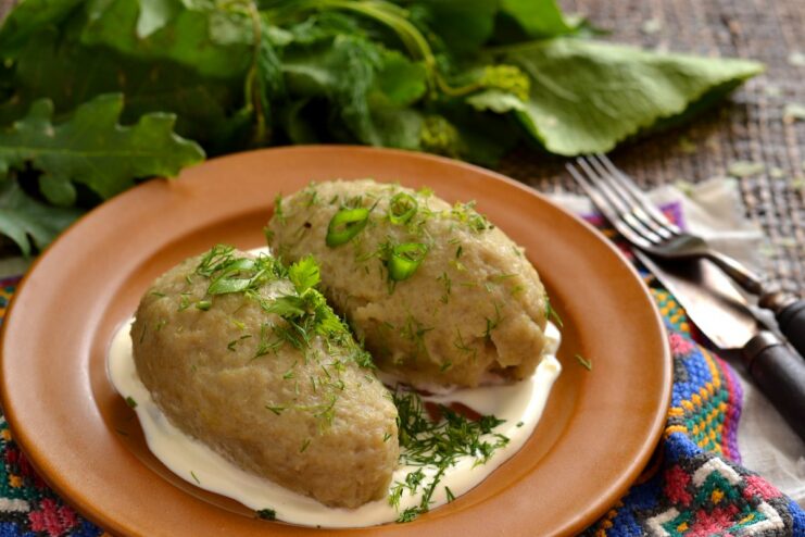A white bowl filled with potato dumplings with meat, garnished with dill and served with sour cream.
